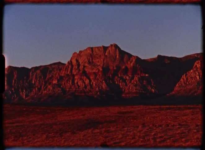 Archival shot of a majestic desert mountain range bathed in the warm, red light of sunrise