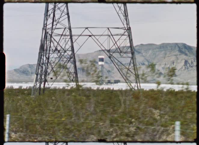 Vintage film captures a drive-by shot of a solar power plant in the desert with mountains in the background