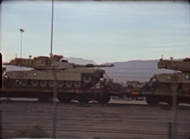 Authentic vintage film captures military tanks being transported on a freight train through an arid, desert landscape