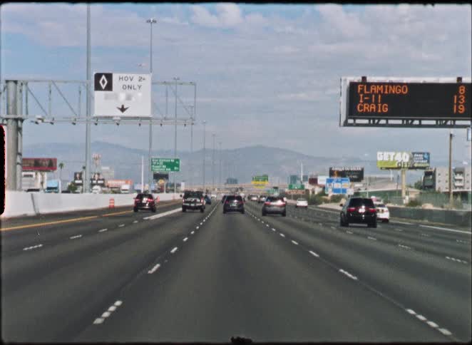 A vintage film-style POV shot of driving on a Las Vegas freeway with mountains visible in the distance