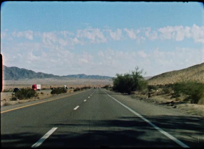 Vintage Super 8 film captures a point-of-view shot driving down a desert highway in the American Southwest