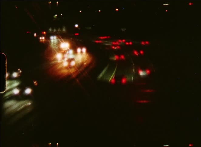 Vintage film captures a blurry time-lapse of car headlights and taillights on a busy highway at night