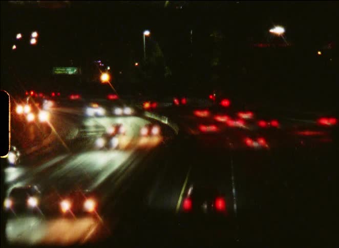 A grainy, vintage-style time-lapse shows streaks of traffic lights speeding along a busy highway at night
