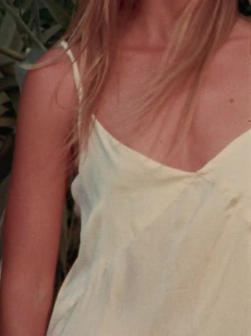 A close-up shot of a blonde woman in a sundress standing amidst tall foliage, captured on vintage film