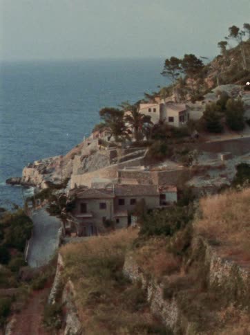 Vintage film captures a scenic view of houses built into a rugged Mediterranean cliffside by the sea