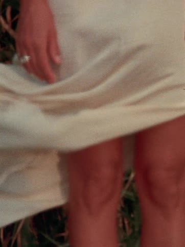 A close-up slow-motion shot captures a white dress gently blowing in the wind against a woman's legs