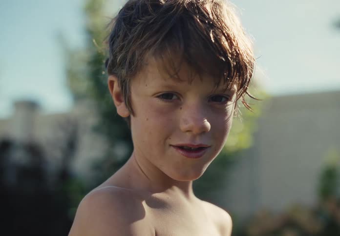 Sunlit close-up portrait of a young boy outdoors looking into the camera with a subtle smile