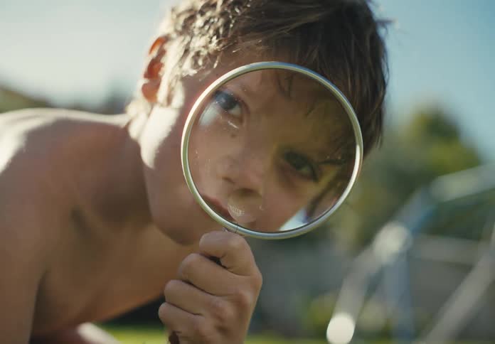Curious young boy examines the world through a magnifying glass in a sunny backyard