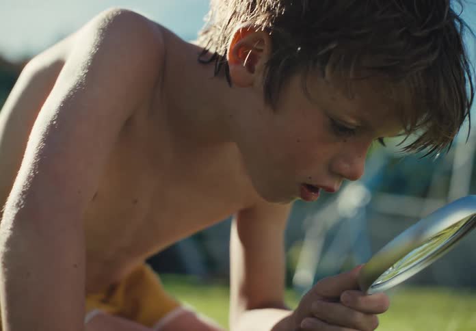 Curious young boy examines the grass outdoors with a magnifying glass in warm sunlight