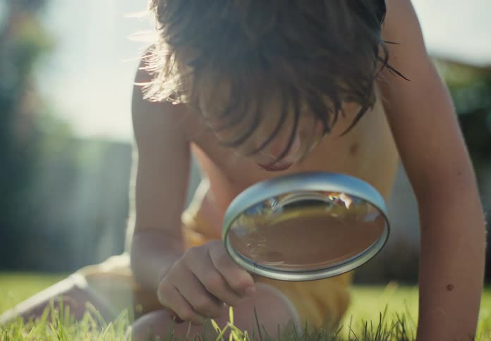 Curious young boy examines grass with a magnifying glass in a sunny backyard