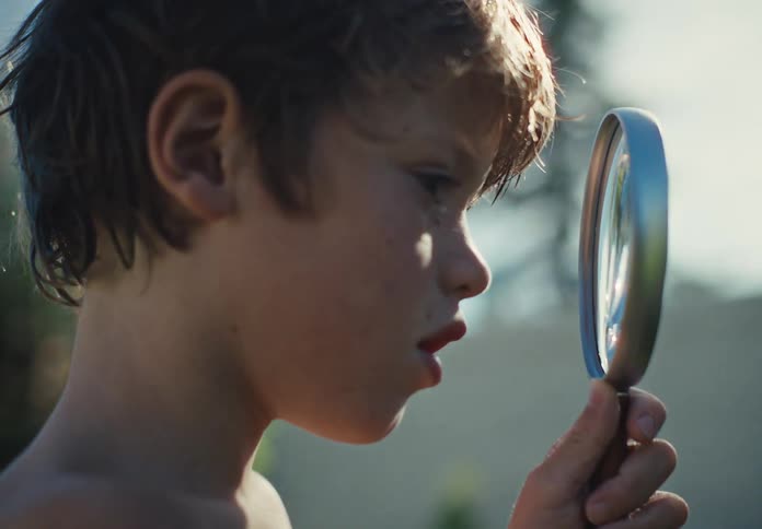 Young boy examines something closely through a magnifying glass outdoors in warm afternoon light