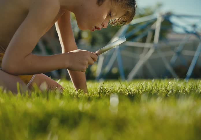 A curious young boy in his backyard uses a magnifying glass to explore the green grass on a sunny summer day