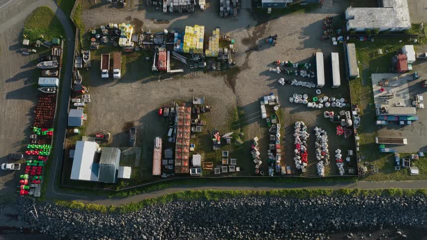 Aerial top-down shot slowly ascends over a coastal industrial yard filled with buoys, traps, and other fishing equipment