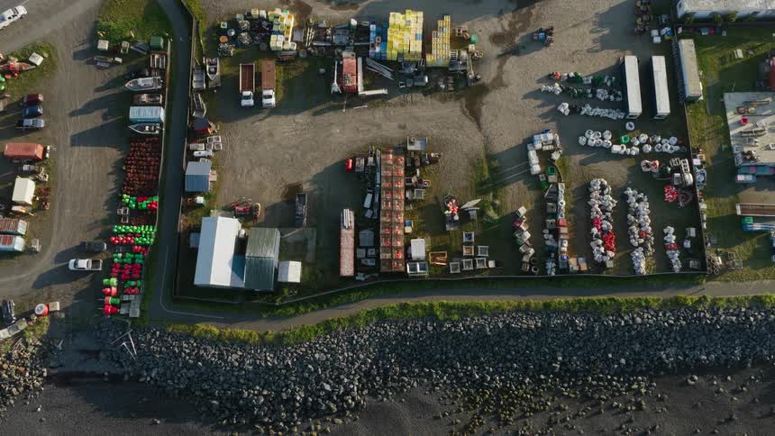 Overhead time-lapse view of a busy commercial fishing yard with equipment, trucks, and boats moving along the rocky coast