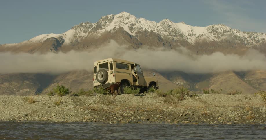 A dog runs over to a jeep by the water