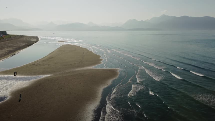 Serene aerial view of a vast, sandy coastline with gentle waves and a hazy mountain range in the background