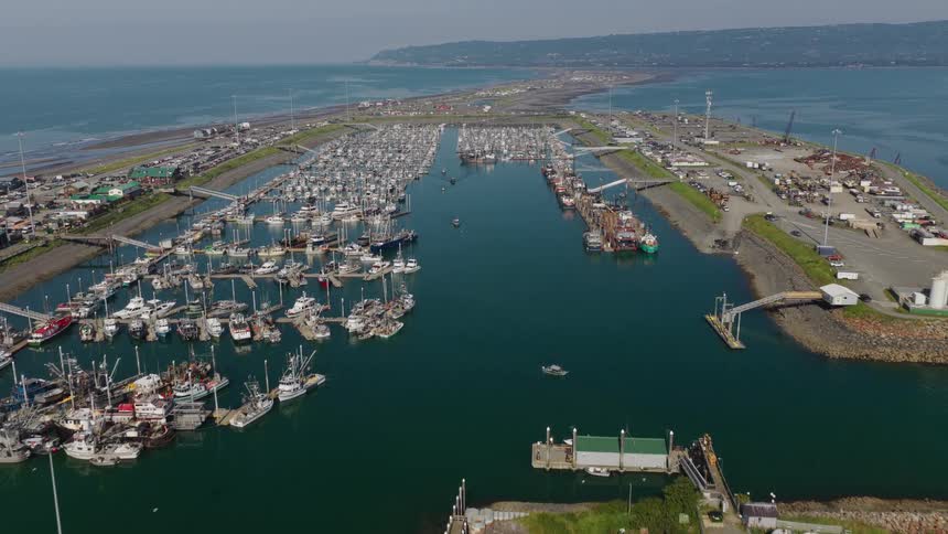 An aerial drone flies over a busy harbor filled with commercial fishing boats and pleasure craft on a sunny day in a coastal town