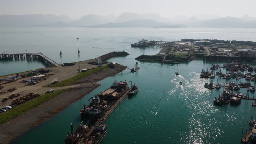 A wide aerial view of a bustling commercial fishing harbor in a scenic coastal town with hazy mountains in the distance