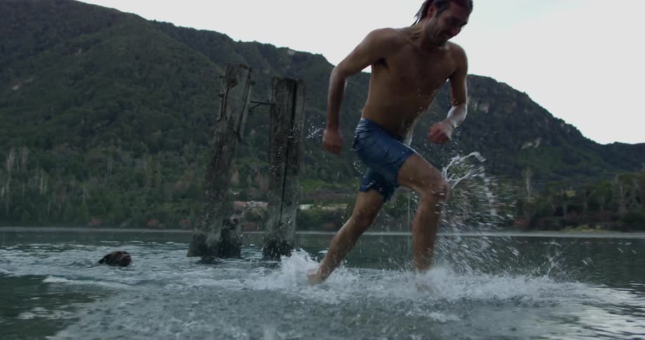 A man runs out of the water with his dog following
