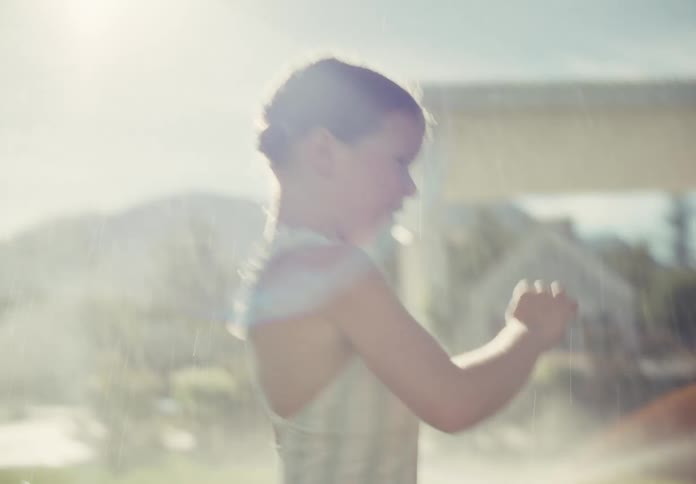 Slow motion of a happy young girl in a swimsuit joyfully running through sprinklers in a sunny backyard