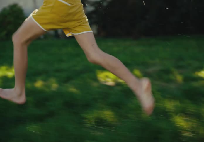 Slow motion side view of a happy boy running barefoot through the wet grass on a sunny summer day in his backyard