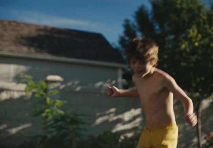 Boy runs shirtless through backyard sprinklers on a sunny summer afternoon