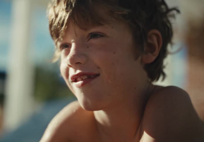Close-up of a happy young boy with wet hair and a missing tooth smiling joyfully in the warm summer sunlight