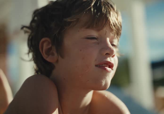 Sunlit close-up portrait of a smiling young boy relaxing outdoors in warm summer light