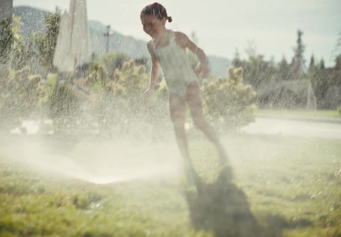 Slow motion shot of two happy children running barefoot through a lawn sprinkler on a sunny summer day