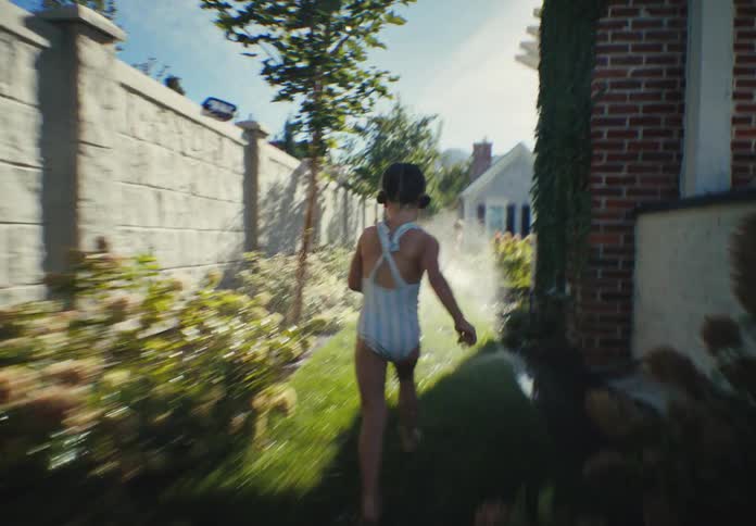 A joyful little girl in a swimsuit runs through sprinklers in her sunny backyard in slow motion