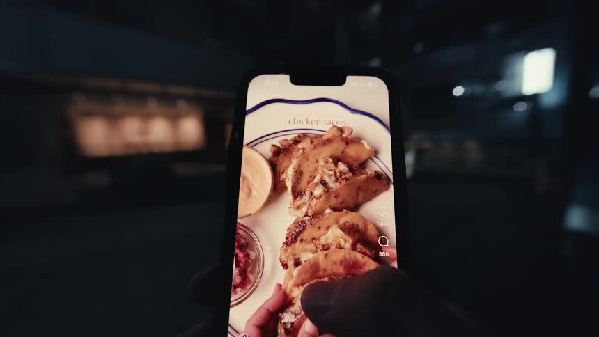 A close-up first-person view of a hand holding a smartphone and scrolling through a social media video feed at night