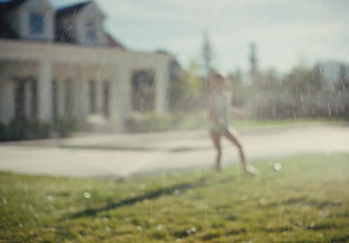 A happy young boy and girl run and play in a backyard sprinkler on a beautiful sunny summer day in slow motion