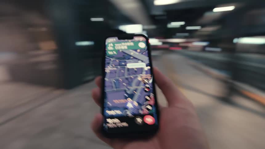 First-person perspective of someone walking through a city at night, using a GPS navigation app on a smartphone to find their way to an escalator