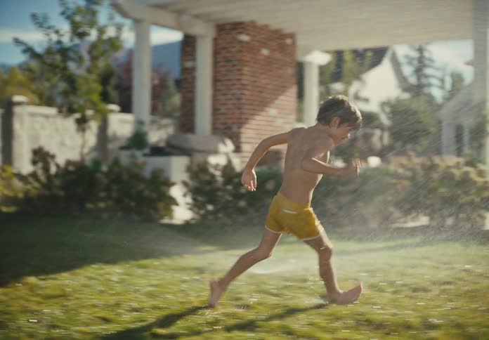 Two happy children in swimsuits run and play in a lawn sprinkler on a sunny summer day in slow motion