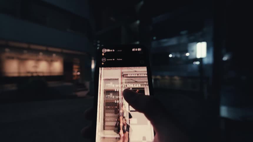 A first-person view of a hand holding a smartphone and endlessly scrolling through a social media video feed at night