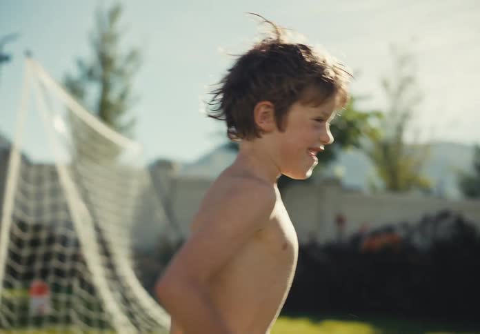 Smiling young boy runs through a sunny backyard near a soccer goal on a warm summer day