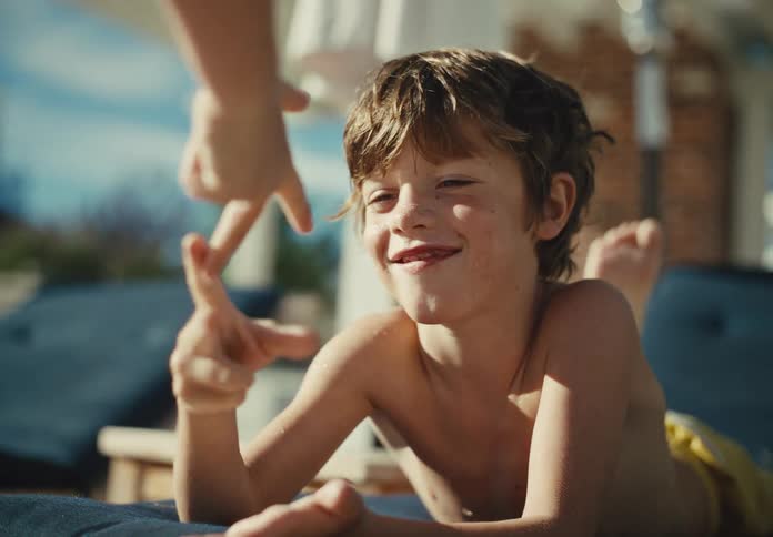 Smiling young boy lounging poolside and playing a hand game in warm afternoon sunlight