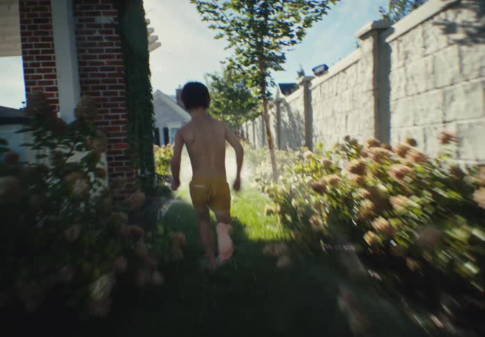 A young boy joyfully runs barefoot through the sprinklers in his lush green backyard on a sunny summer day in slow motion