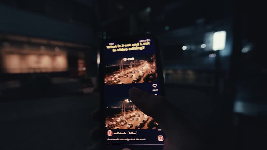 A point-of-view shot of a hand holding a smartphone and endlessly scrolling through a social media feed at night