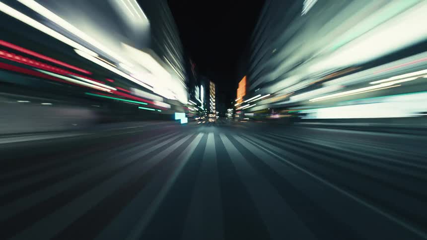 A low-angle hyperlapse perspective of racing through an urban metropolis at night, with city lights blurring into streaks