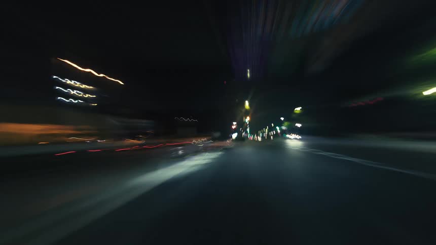 An abstract first-person hyperlapse shows streaks of colorful city lights while driving at high speed through streets and tunnels at night