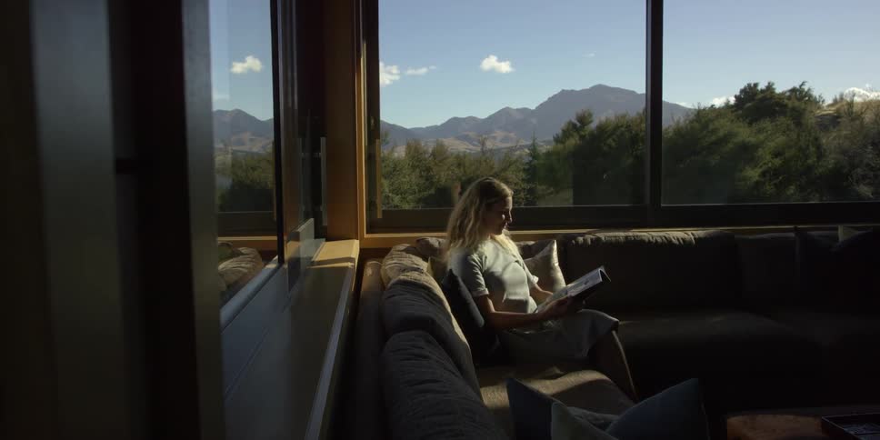 Woman reading on a couch surrounded by large windows