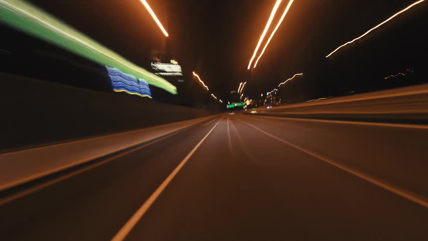 An abstract POV hyperlapse of driving through a city at high speed at night, with blurred light trails creating a dynamic effect