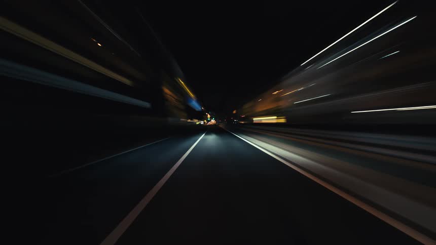 Futuristic POV time-lapse of driving at high speed through a city at night creating vibrant light trails