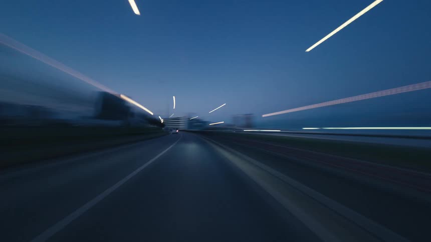 A dynamic hyper-lapse POV of driving through a modern city at dusk, with lights streaking past