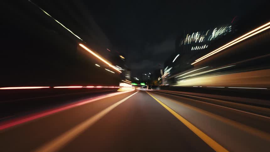 An exhilarating point-of-view hyper-lapse of driving through a bustling city and tunnels at night, with light trails from cars and buildings