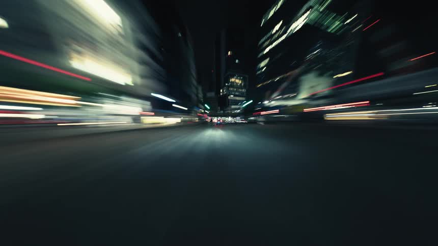 A futuristic point-of-view hyperlapse captures the fast-paced energy of driving through a vibrant, neon-lit city at night