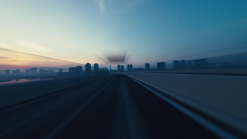 A high-speed, motion-blurred POV hyperlapse shows a drive across a large suspension bridge into a city at sunrise