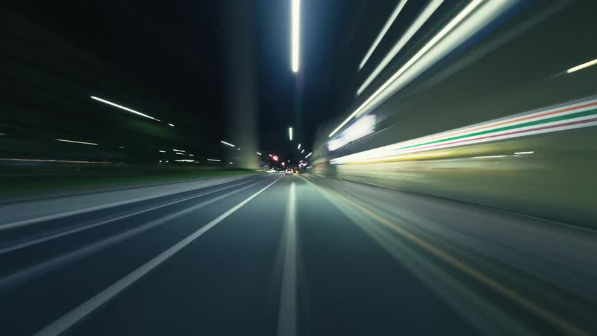 A point-of-view hyperlapse of driving down a city street at night, with the surrounding lights creating colorful streaks of motion blur