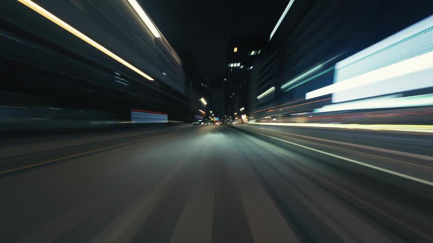 A dynamic point-of-view time-lapse shows a fast drive through city streets at night, with colorful light trails streaking across the screen